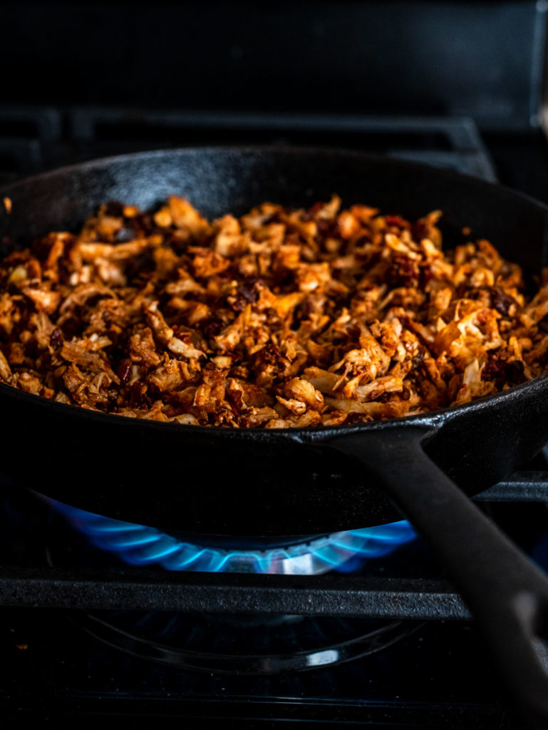 Shredded chicken cooking in a cast-iron skillet for the Chicken Chipotle Nachos.